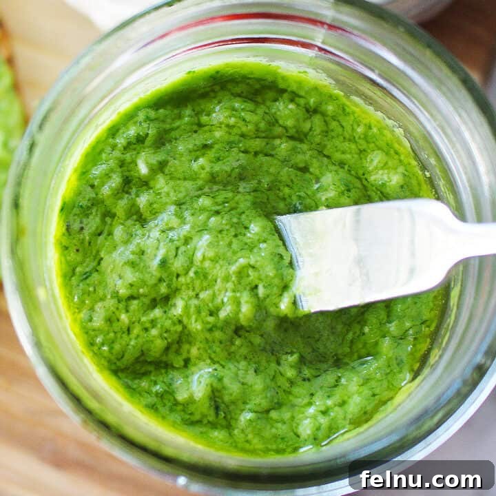 Creamy Avocado Pesto 10 bright green avocado pesto in a mason jar with a small knife placed in the pesto.
