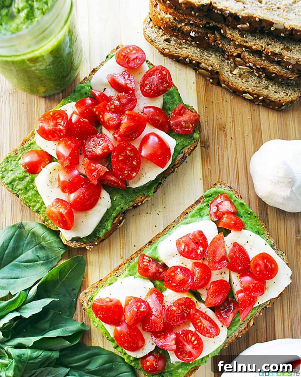 Creamy Avocado Pesto 9 two pieces of pesto, cheese, tomato toast on a cutting board with slices of bread in one corner and spinach leaves in another corner.