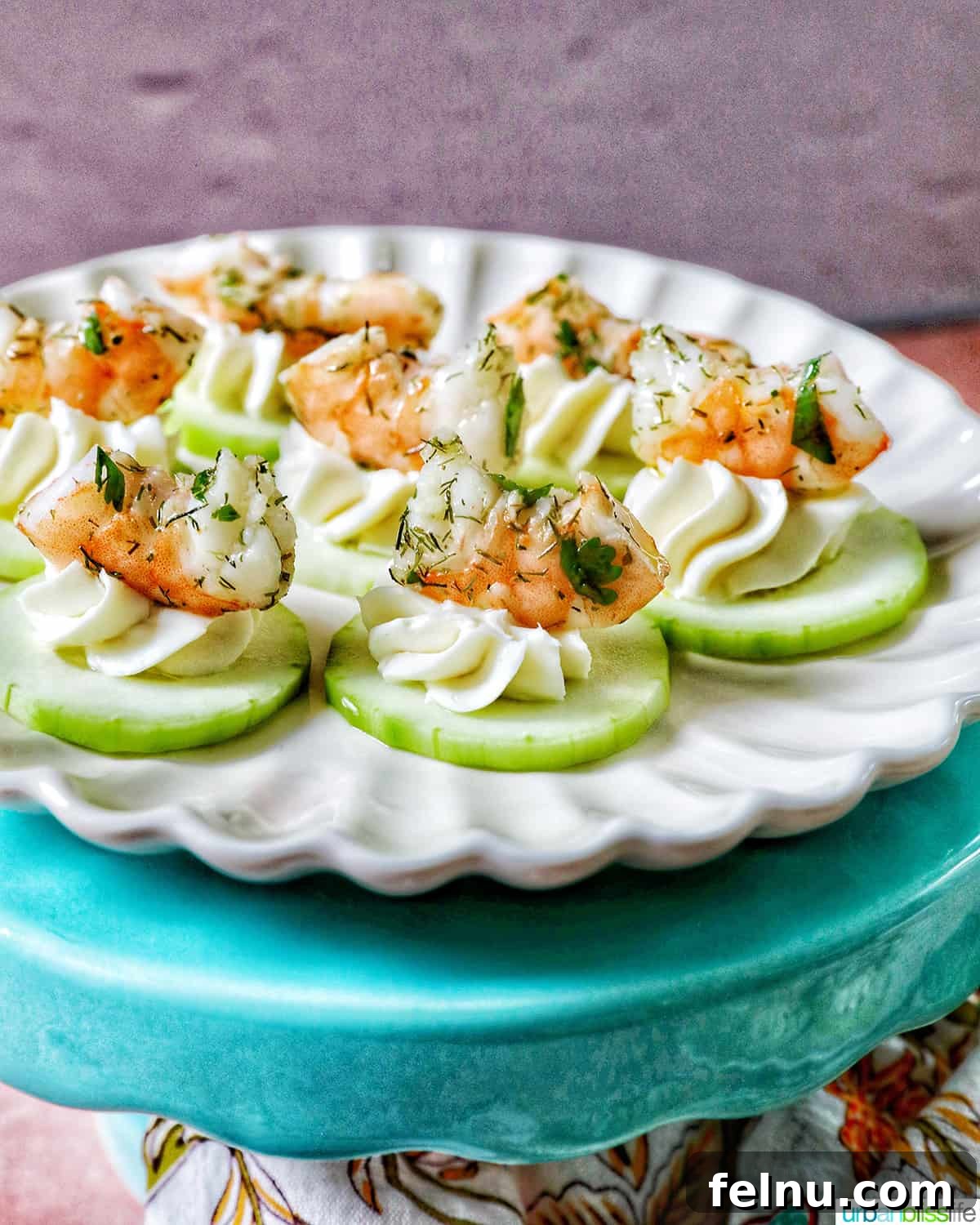 Crisp Cucumber Shrimp Delights 2 Elegant cucumber shrimp canapé appetizers presented on a white plate on a blue pedestal, ready for a party.