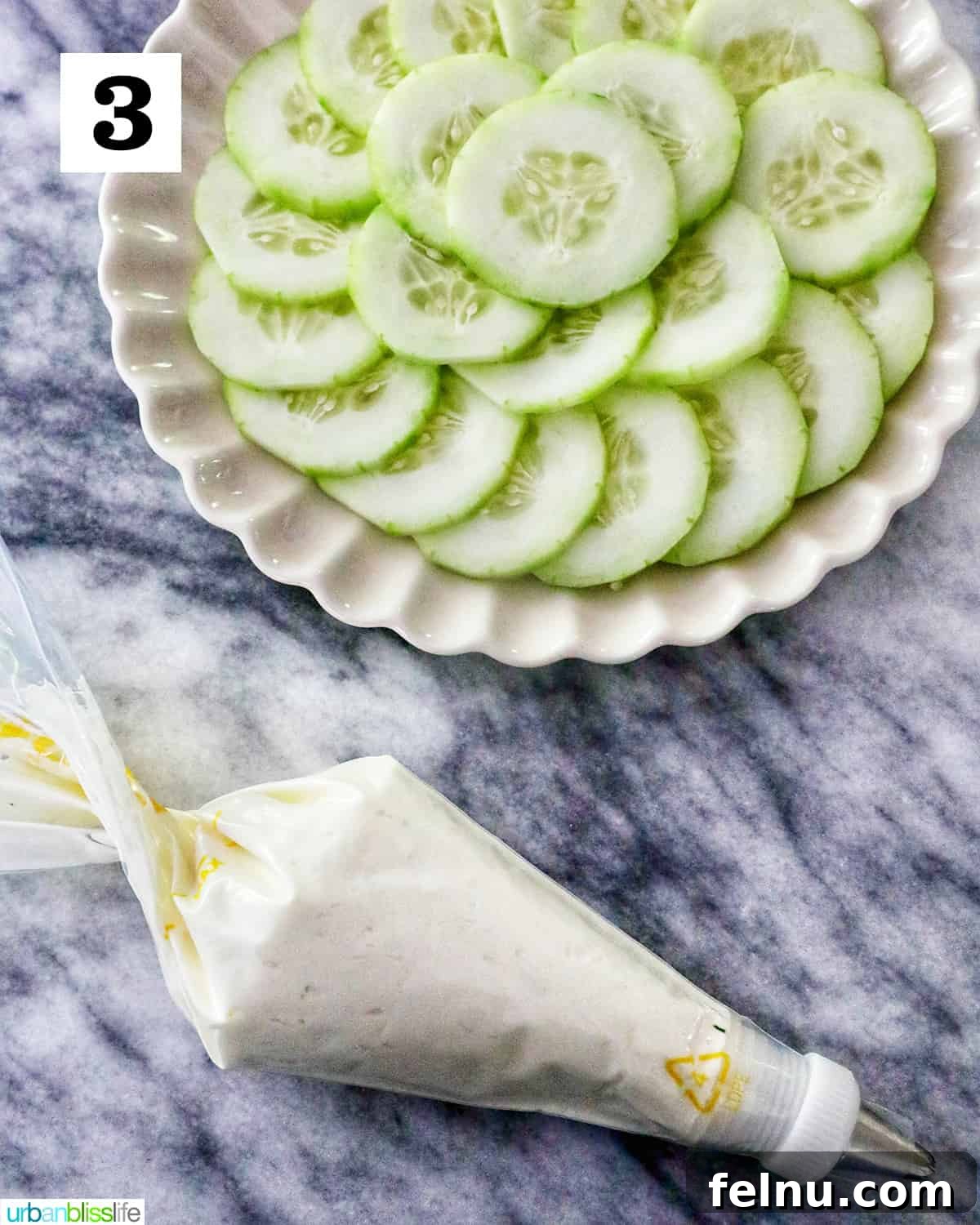 Crisp Cucumber Shrimp Delights 7 A plate featuring fanned-out cucumber slices next to a piping bag filled with cream cheese on a marble countertop, ready for assembly.
