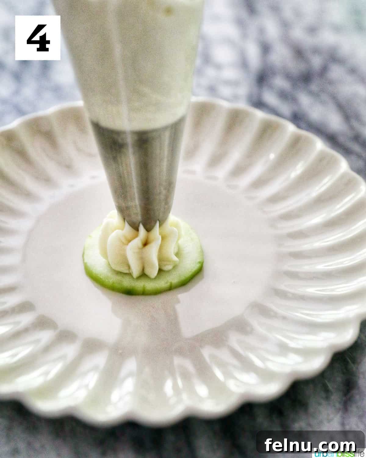 Crisp Cucumber Shrimp Delights 8 Cream cheese being piped from a pastry bag onto a single cucumber slice resting on a scalloped plate, forming a soft peak.