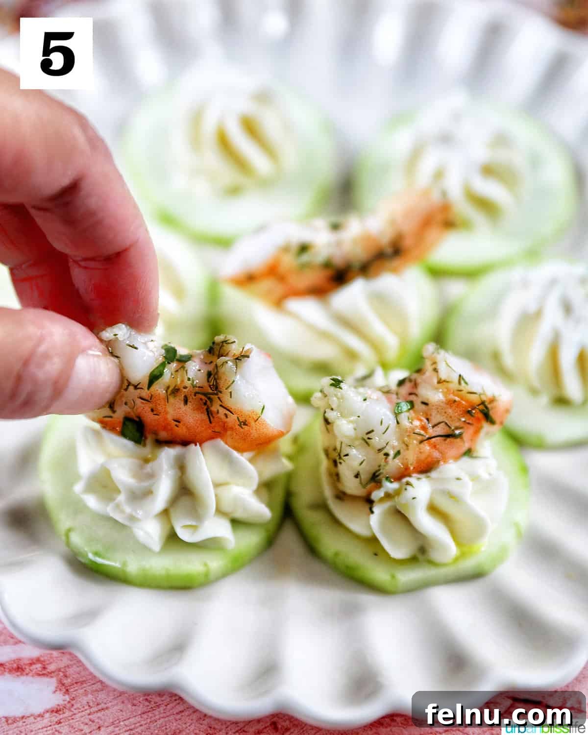Crisp Cucumber Shrimp Delights 10 A hand carefully placing a marinated shrimp onto a cucumber cream cheese canapé appetizer on a scalloped plate, completing the assembly.