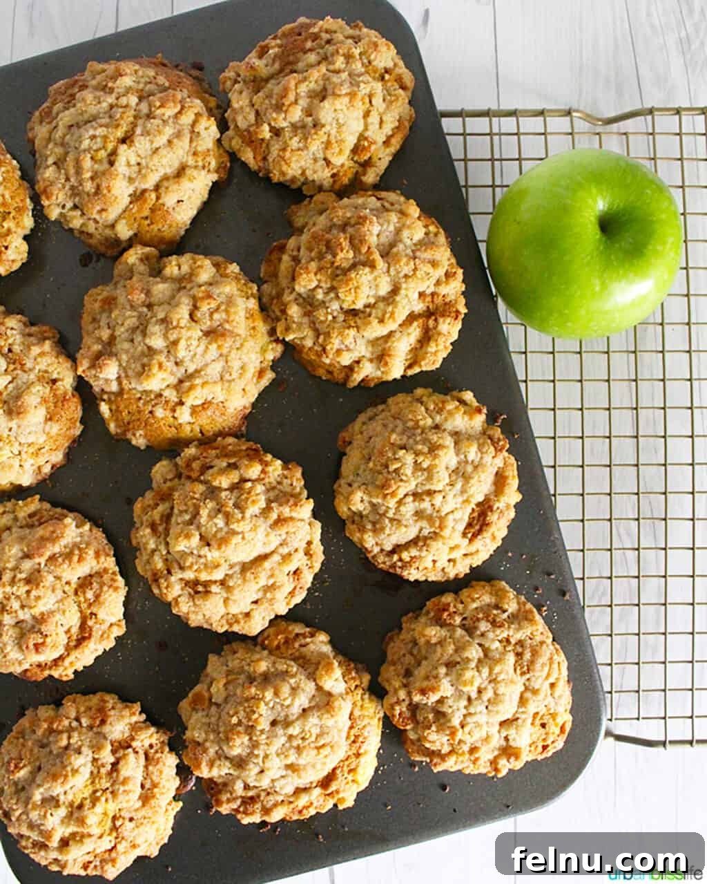 Cinnamon Apple Crumble Muffins 6 A muffin tin filled with baked cinnamon streusel muffins, with a green apple on the side.