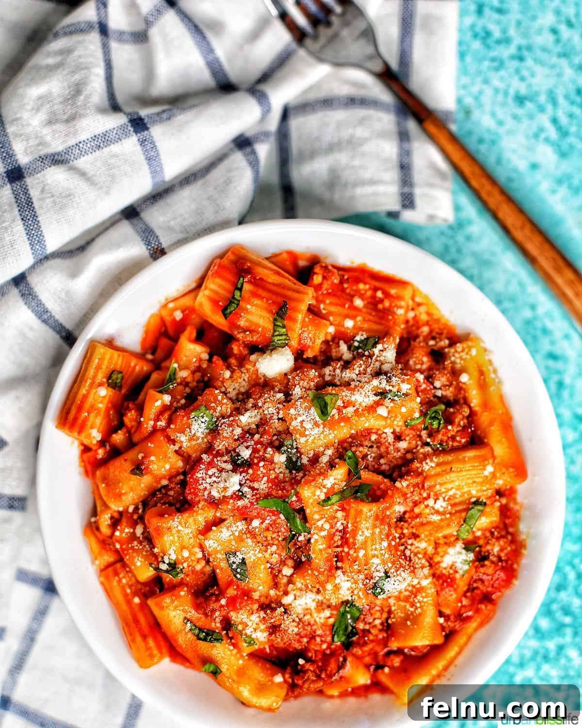 Effortless Italian Sausage Rigatoni Delight 2 Rigatoni pasta with Italian sausage served on a white and blue checkered napkin with a fork.