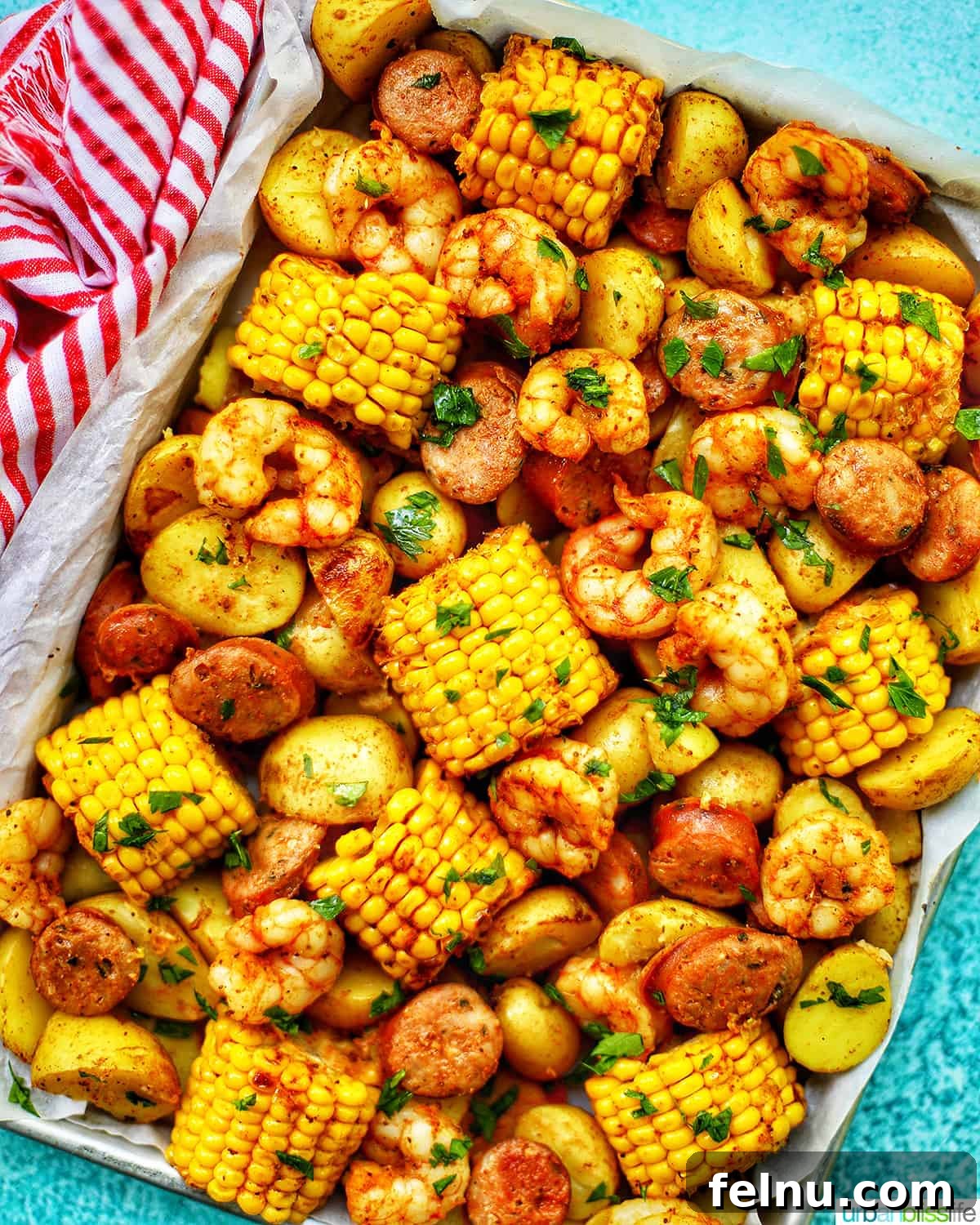 Sip, Sizzle, Savor: Wines That Perfect Your BBQ 19 A bountiful tray filled with a seafood boil, featuring corn, sausage, and various seafood, set against a blue background with a charming red and white towel.