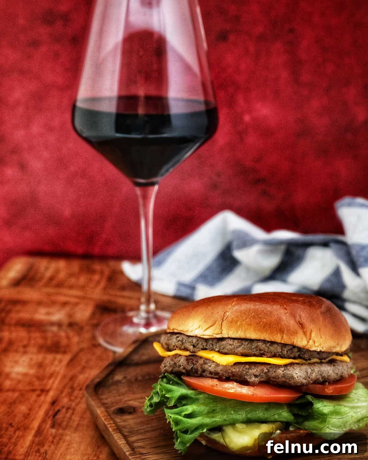 Sip, Sizzle, Savor: Wines That Perfect Your BBQ 7 A vibrant glass of Malbec red wine is prominently featured behind a wooden tray, which holds a fully loaded burger, all set against a striking red background.