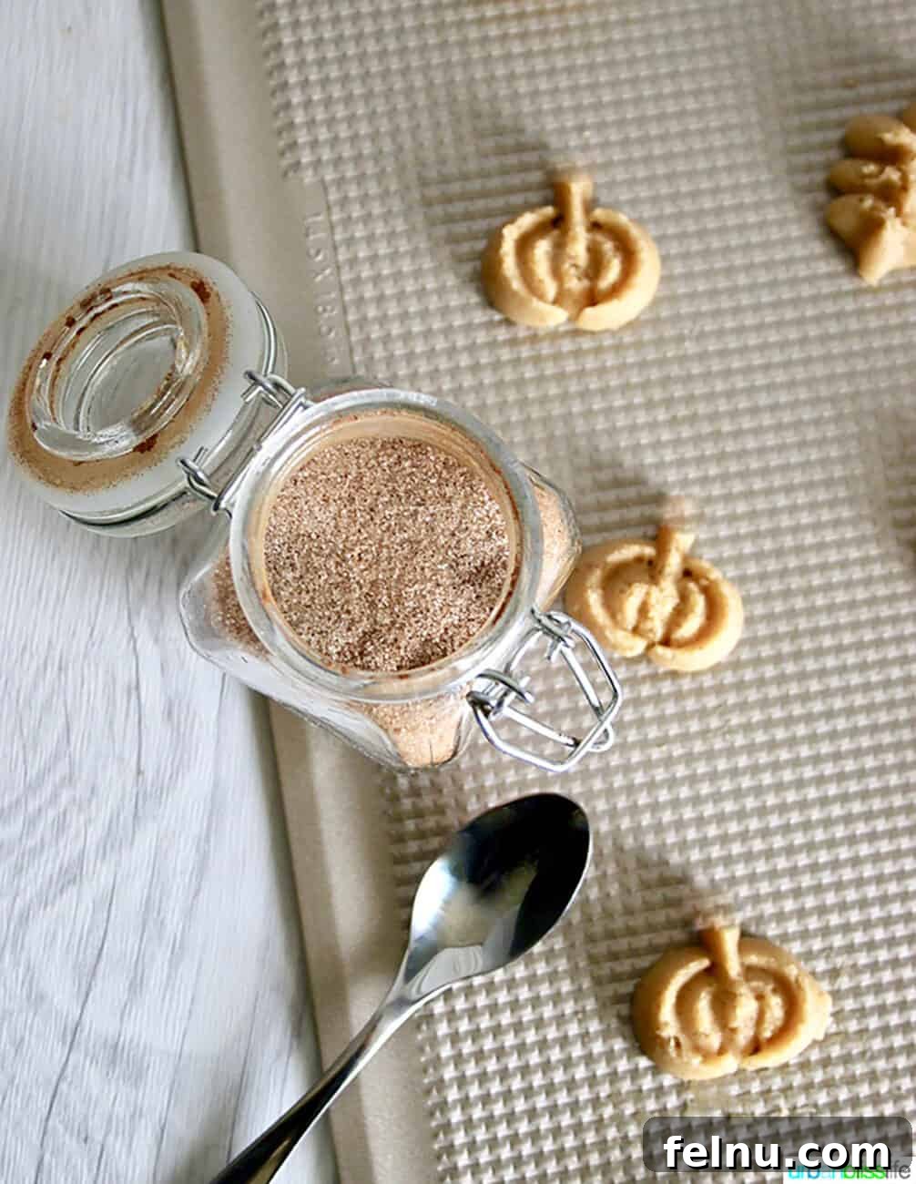 Maple Cinnamon Spritz Delights 3 Spritz Cookies on a baking sheet with jar of cinnamon sugar
