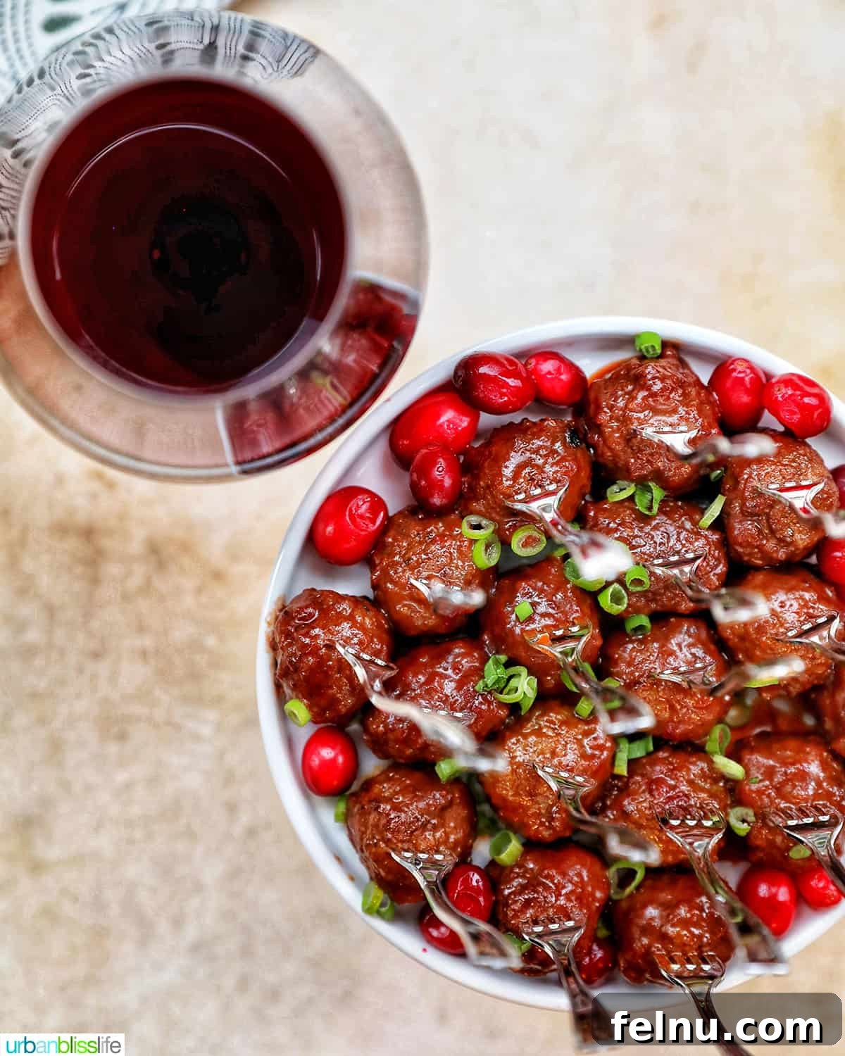Sweet and Tangy Cranberry Glazed Meatballs 13 red wine glass next to plate of cranberry meatballs with a festive background