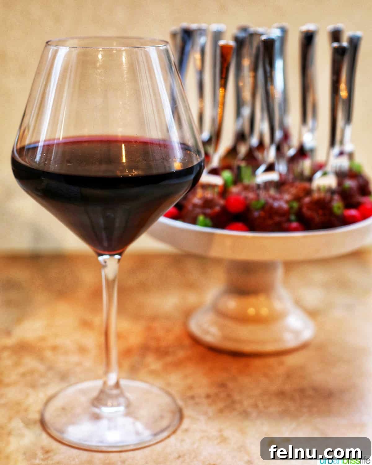 Sweet and Tangy Cranberry Glazed Meatballs 17 red wine glass with cake stand full of cranberry meatballs on a festive table setting