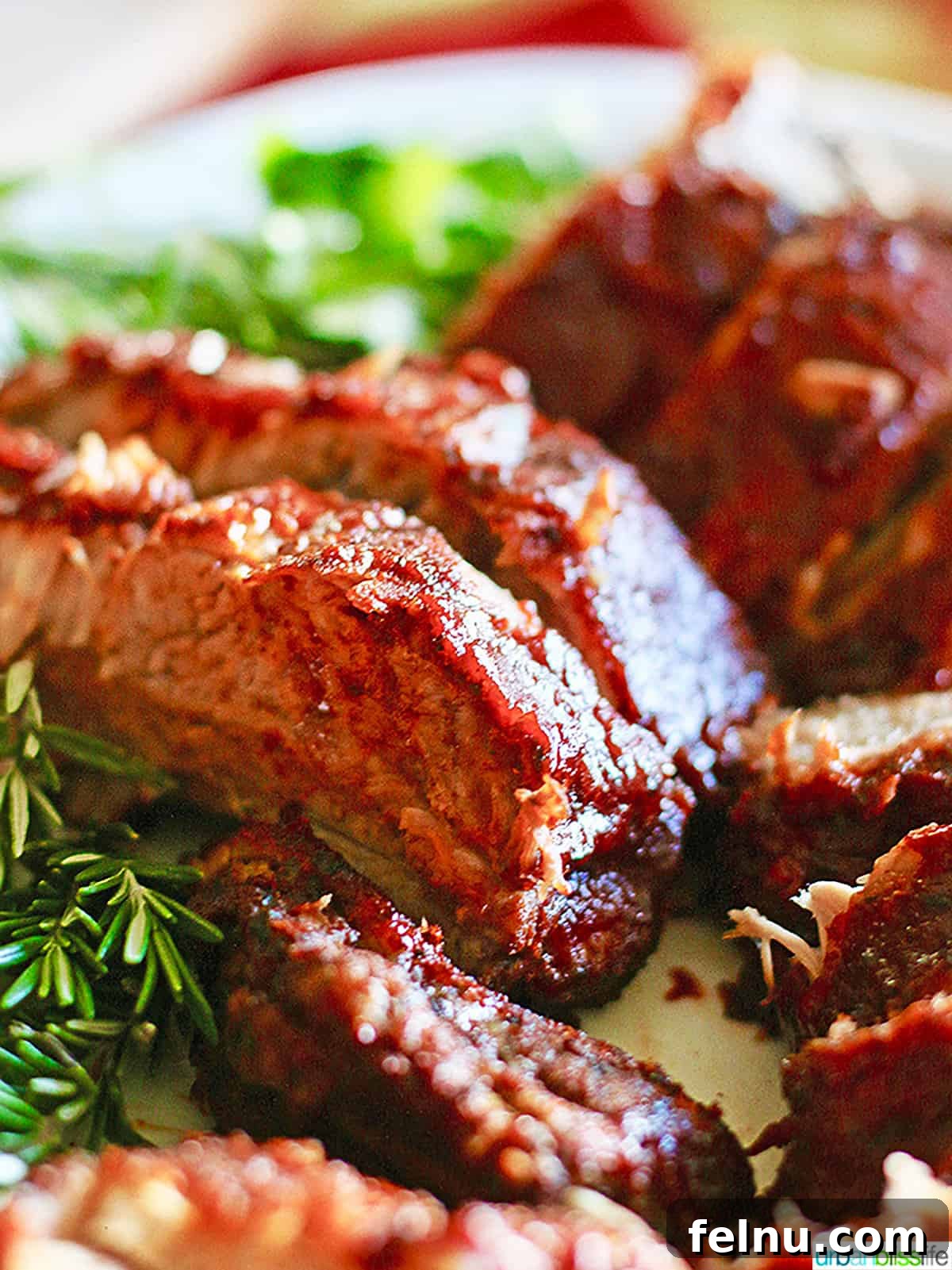 Fall-Off-The-Bone Instant Pot Ribs with Homemade BBQ 3 Plate full of sliced Instant Pot pork ribs with rosemary and other herbs, viewed from a side angle.