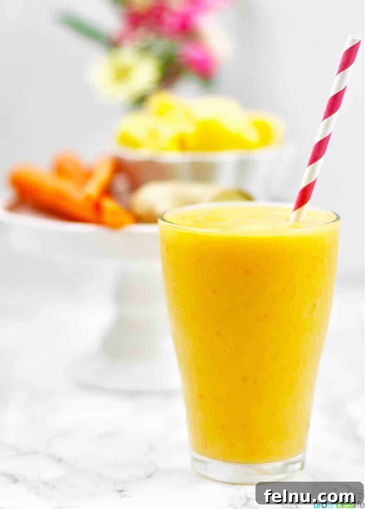 Mango Carrot Elixir 2 A vibrant mango carrot smoothie served in a glass with a red and white straw