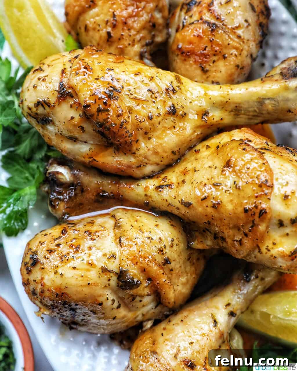 30 Must-Try Whole30 Recipes 12 Stack of chicken drumsticks with seasoning and garnished with parsley and side of lemon wedges on bed of herbs.