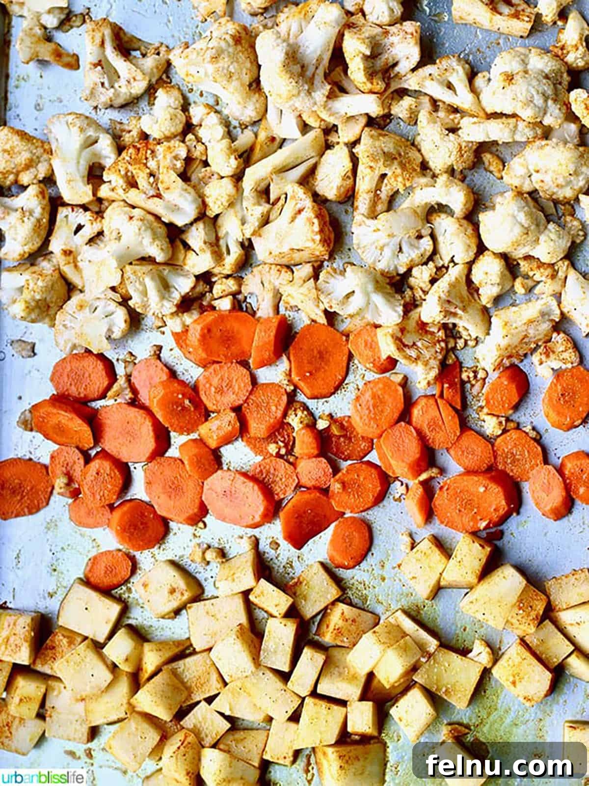 Golden Carrot Cauliflower Puree 4 A sheet pan loaded with meticulously chopped and seasoned cauliflower florets, vibrant carrot slices, and perfectly diced potatoes, ready for roasting. The spices are visible, promising a flavorful outcome.