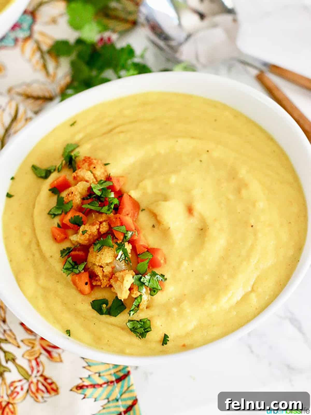 Golden Carrot Cauliflower Puree 5 A pristine white bowl filled with the inviting Creamy Cauliflower Carrot Soup, beautifully garnished with a sprinkle of fresh chopped cauliflower, delicate carrot pieces, and vibrant parsley, ready to be enjoyed.