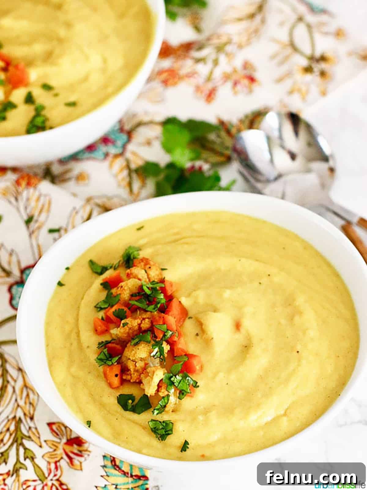 Golden Carrot Cauliflower Puree 6 A close-up of a white bowl overflowing with the delectable Cauliflower Carrot Soup, artfully adorned with small pieces of fresh cauliflower, shredded carrots, and a sprig of green parsley, emphasizing the soup's wholesome texture and presentation.