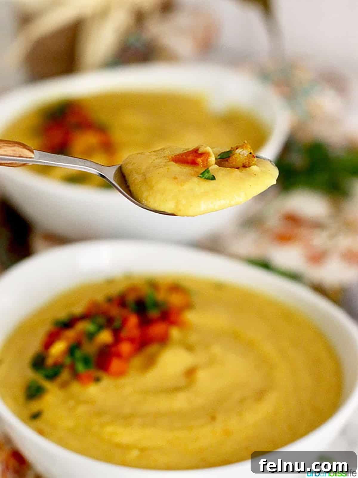 Golden Carrot Cauliflower Puree 8 A spoon lifting a creamy, golden spoonful of Vegan Cauliflower Soup from a pristine white bowl, showcasing its rich texture and inviting warmth. The background blurs to a full bowl of soup, hinting at more deliciousness.