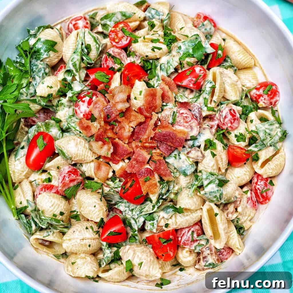 BLT pasta salad in a white bowl on an aqua checkered tablecloth.