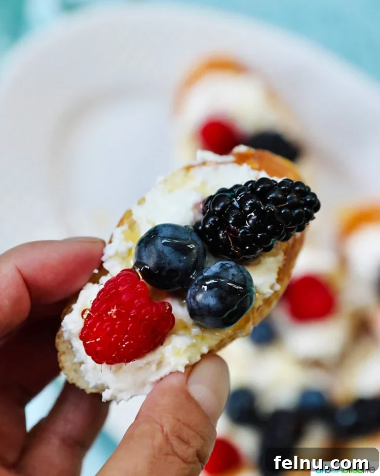 Ricotta Crostini Topped with Summer Berries and Honey Drizzle 4 Holding a single summer berry crostini