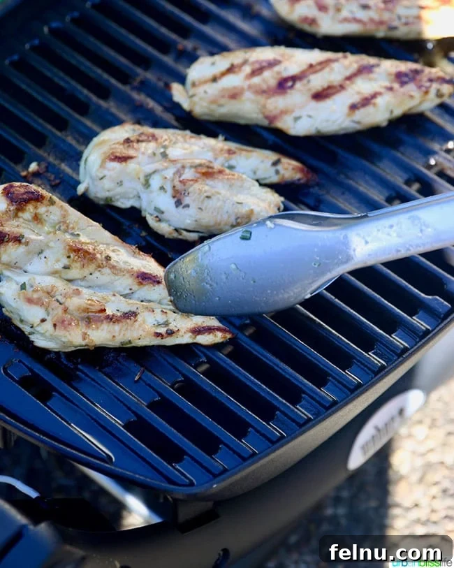 Zesty Lemon Pepper Grilled Chicken 8 Tongs picking up a piece of perfectly grilled lemon pepper chicken from the grill.
