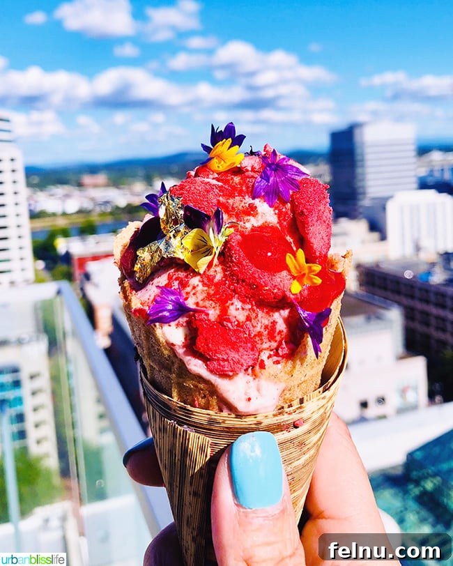Cool Summer Dairy-Free Ice Cream at Departure Portland 2 A vibrant scoop of dairy-free coconut ice cream with a fermented berry swirl, adorned with freeze-dried berries, gold leaf, and edible flowers, presented in a vegan cone.