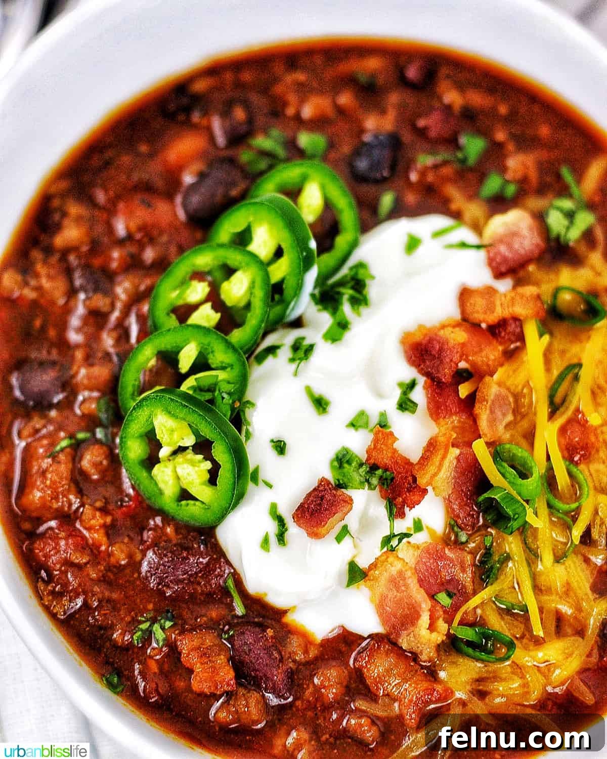 Hearty & Healthy Turkey Chili (Instant Pot Friendly!) 2 A close-up shot of a bowl of Instant Pot Turkey Chili, generously topped with jalapenos, sour cream, crispy bacon, and shredded cheddar cheese.
