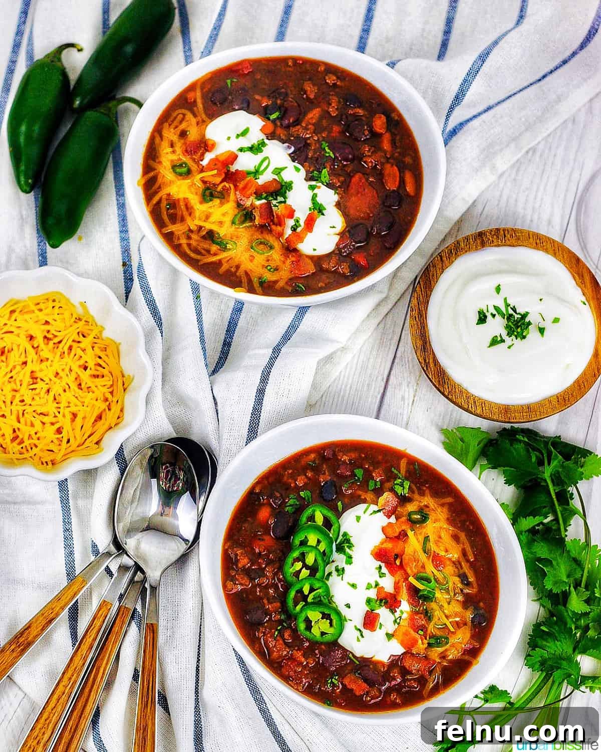 Hearty & Healthy Turkey Chili (Instant Pot Friendly!) 22 Two bowls of Instant Pot Turkey Chili on a white and blue napkin, accompanied by sides of shredded cheddar cheese, jalapenos, and sour cream.