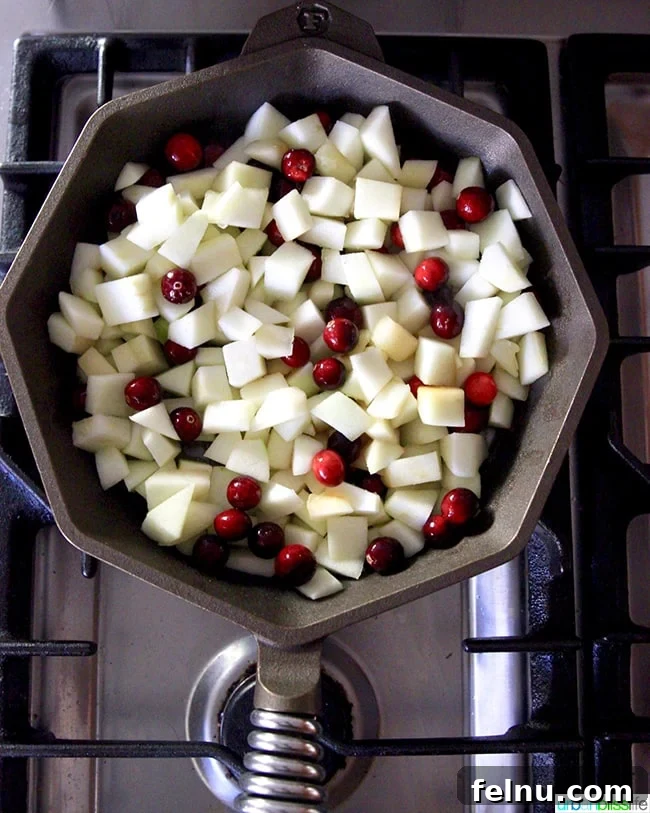 Granny Smith apples and fresh cranberries mixed in a cast iron skillet, ready to be cooked for the crisp filling.
