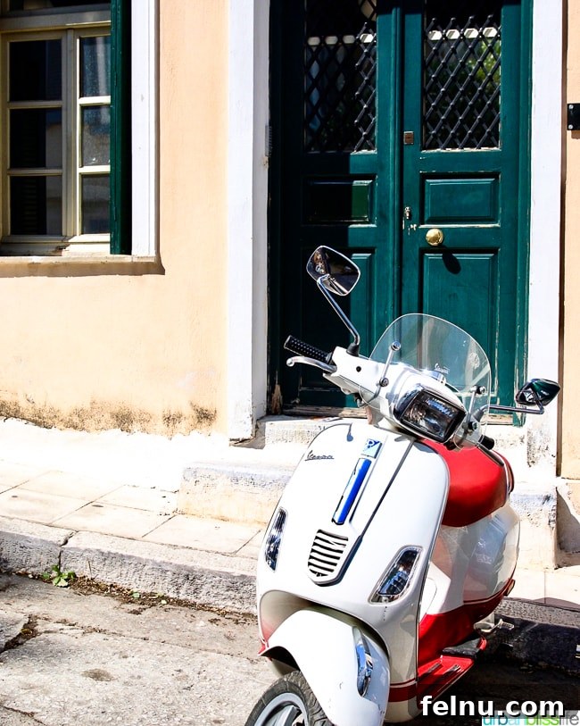 A classic white Vespa parked in front of a building with a green door in Athens, Greece, a quintessential Athenian scene