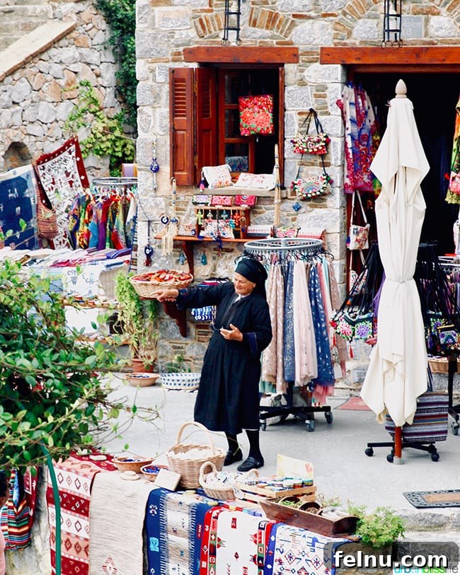 Greece Travel: Discover Olympos Village, Karpathos 11 A woman dressed in black stands in a market surrounded by colorful textiles in Olympos, Karpathos