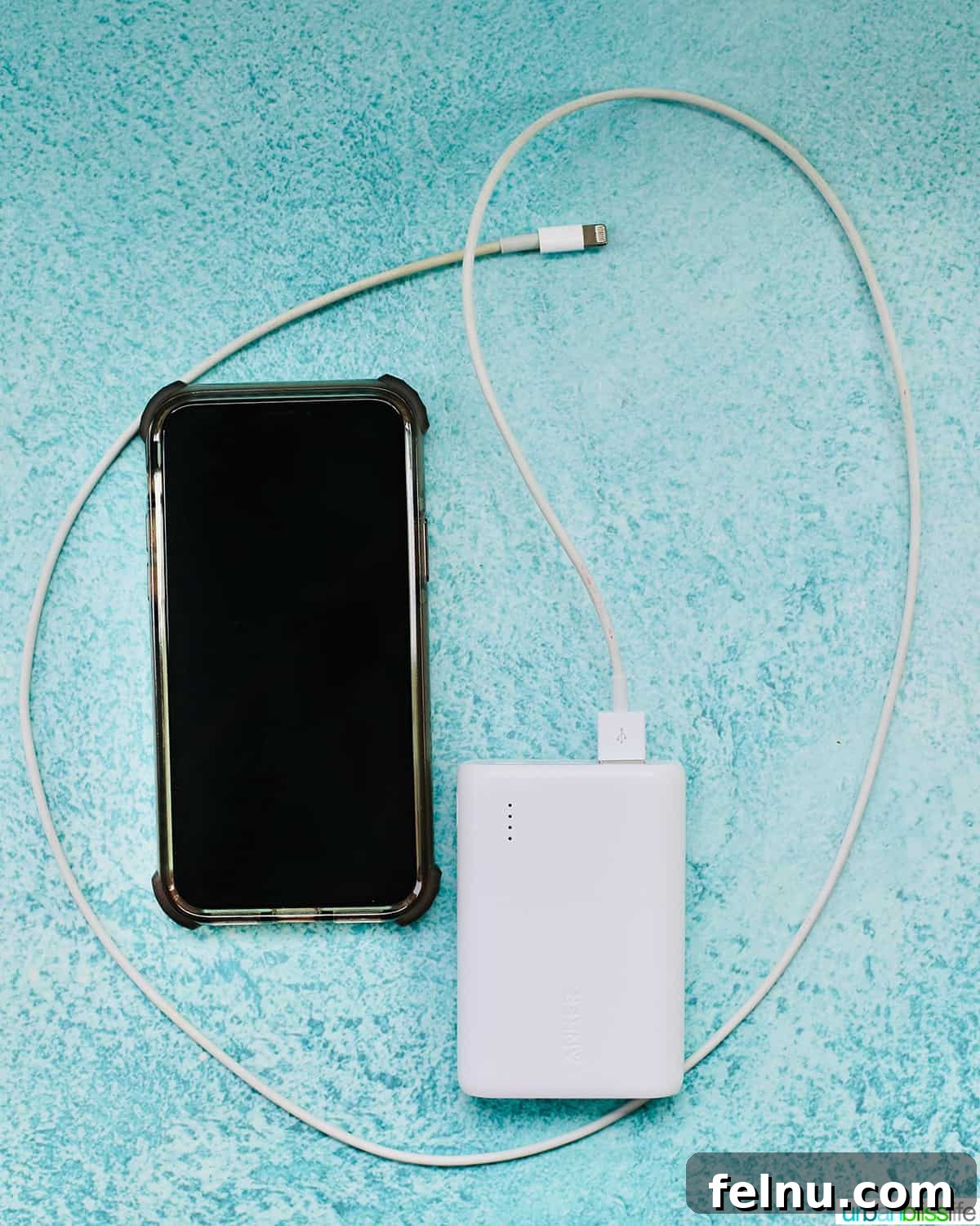 Autumn Drives: Essential Packing List 7 Cell phone with portable charger and phone lightning cord on blue table, essential travel technology for road trips.