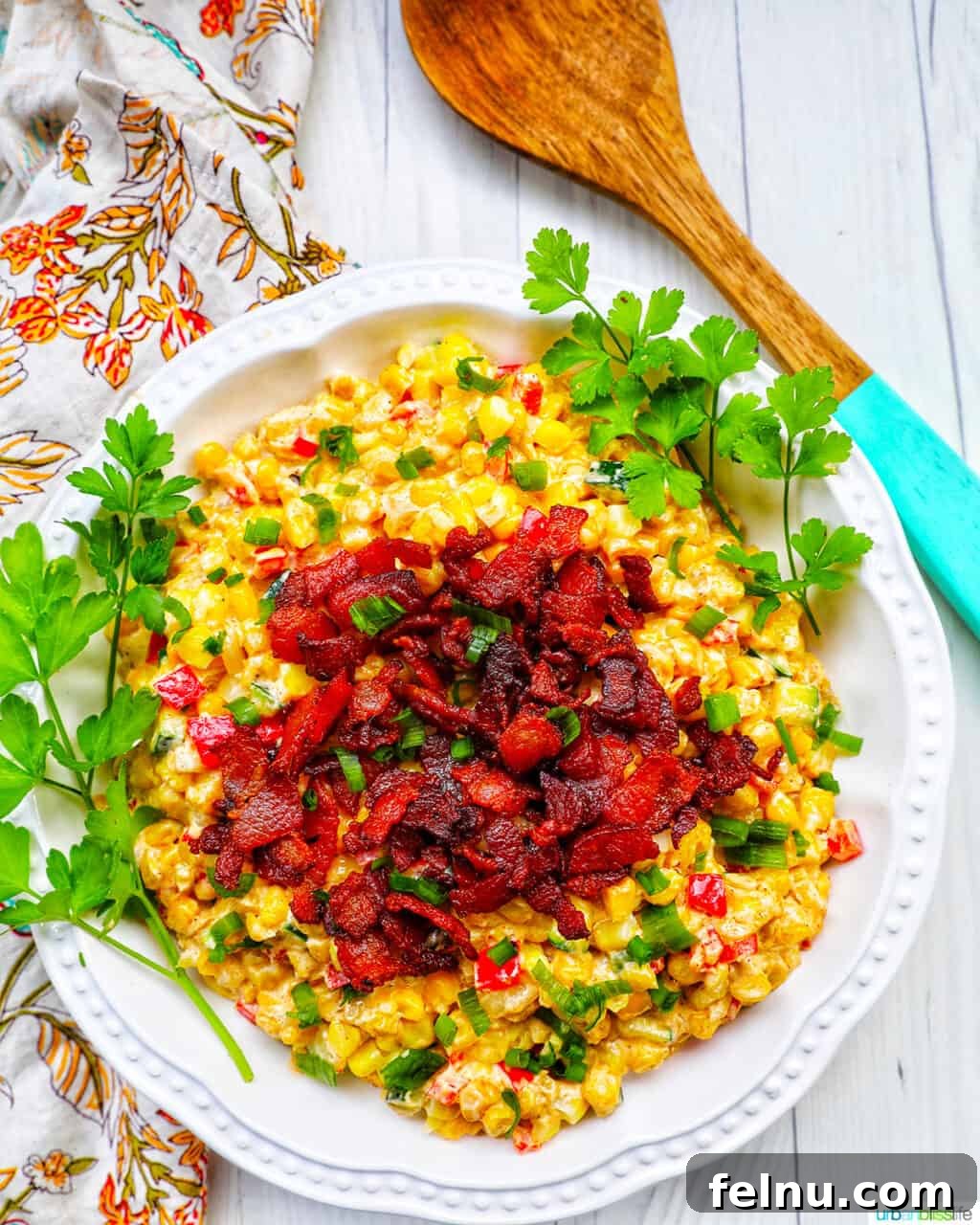 Creamy Kaleidoscope Corn 3 creamy confetti corn with crispy bacon, green onions, peppers, in a white bowl with greens and wooden spoon.