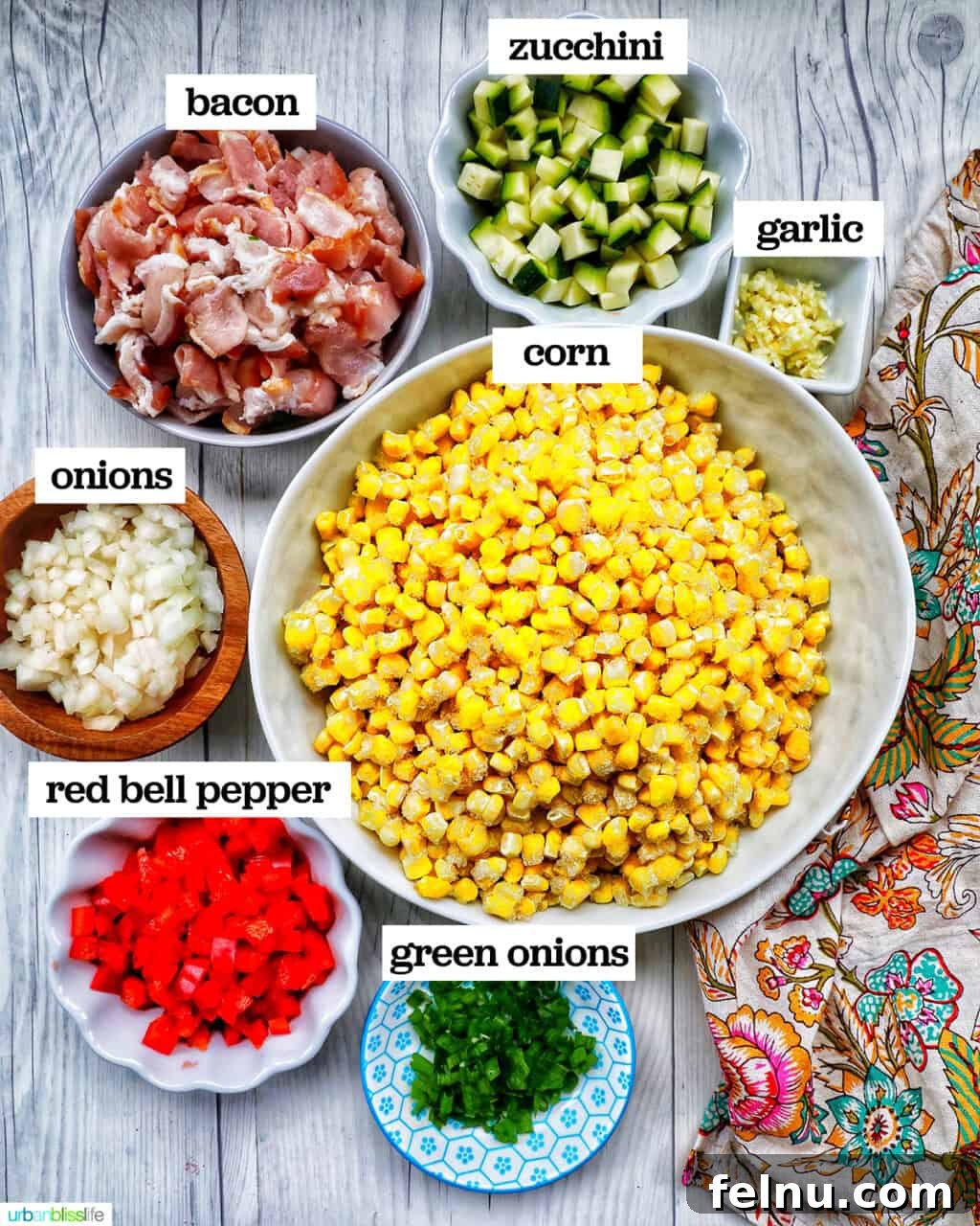 Creamy Kaleidoscope Corn 4 bowls of corn, peppers, zucchini, and other ingredients to make creamy confetti corn salad with a floral napkin.