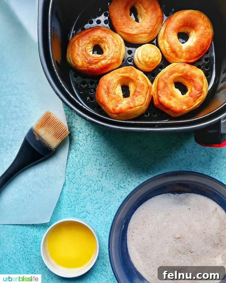 Effortless Air Fryer Doughnuts 4 air fried donuts being dipped into a bowl of cinnamon sugar
