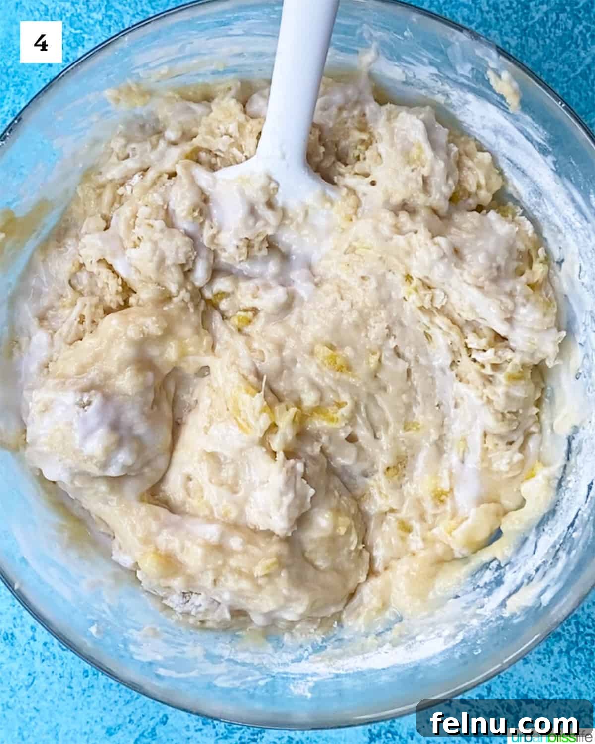 Pineapple Loaf 9 spatula stirring dry ingredients into wet ingredients in a large glass bowl to make pineapple bread.