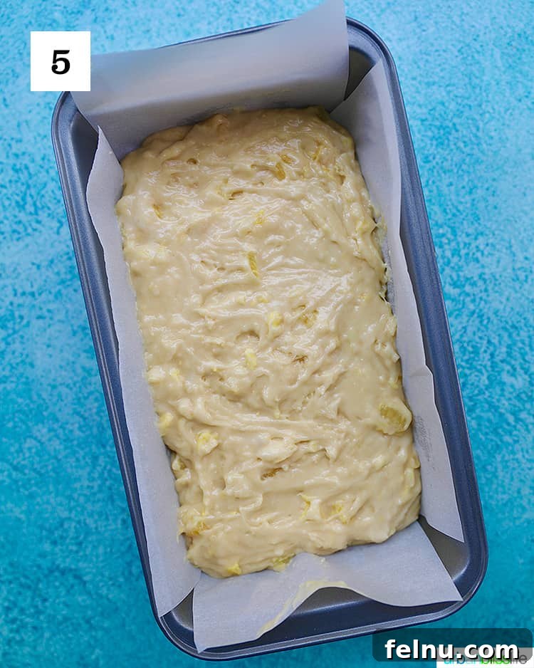 Pineapple Loaf 10 pineapple bread batter poured into a parchment paper-lined baking loaf pan on blue background.