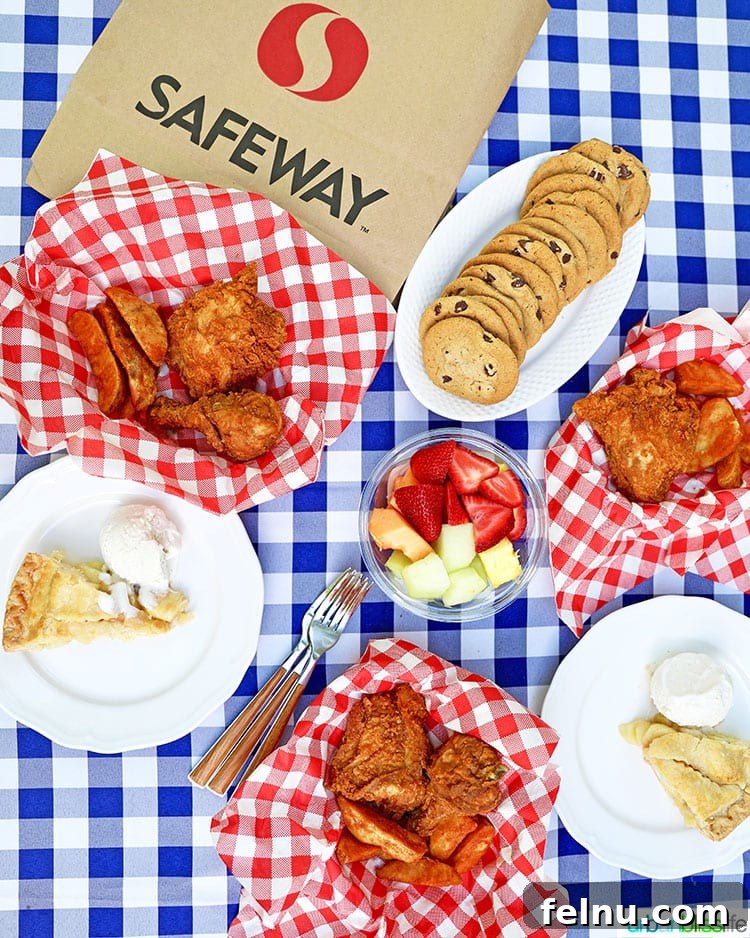 Vibrant summer outdoor picnic with golden fried chicken, crispy jo jos, fresh fruit, and cookies artfully arranged on a classic blue and white checkered tablecloth, with a Safeway bag subtly in the background.