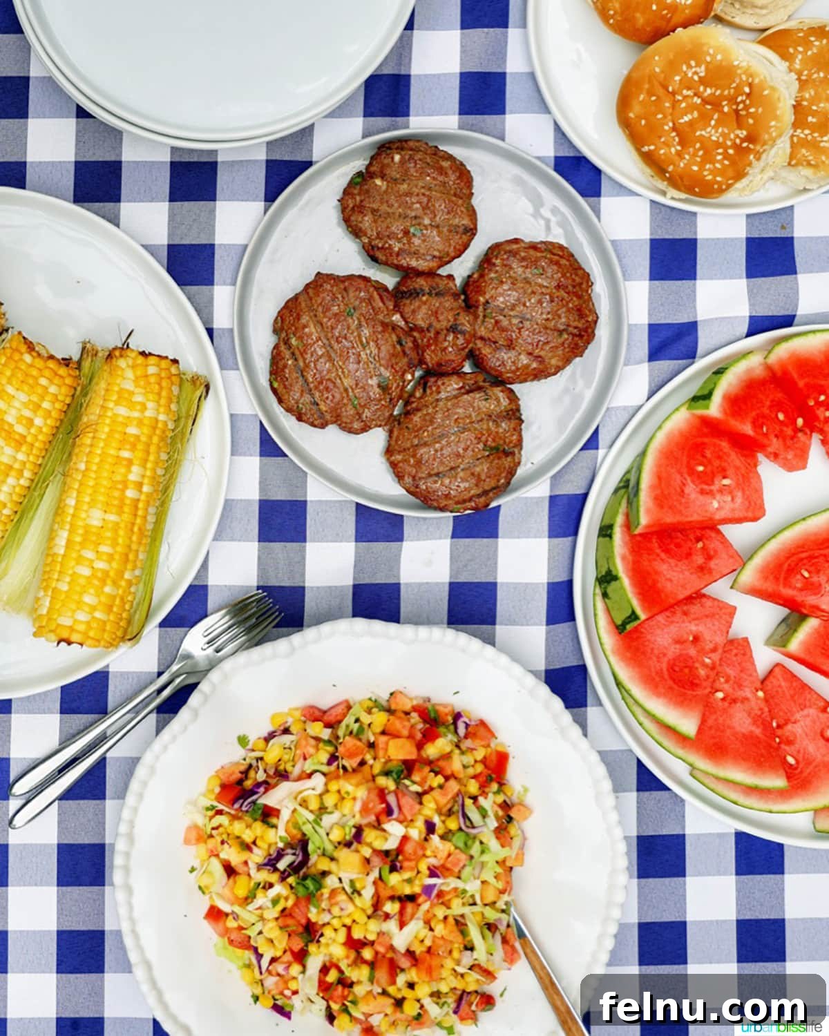 Asian burgers served with slaw, grilled corn on the cob, watermelon slices, and buns for a complete meal.