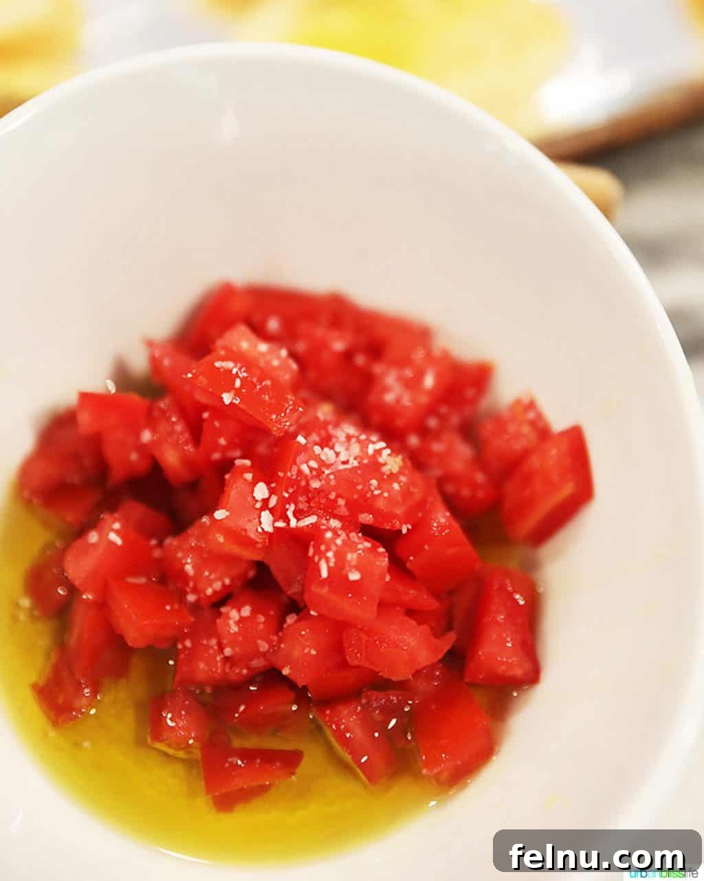Vine-Ripened Tomato Bruschetta with Balsamic Glaze 4 Close-up of chopped tomatoes being mixed with olive oil and herbs in a bowl.