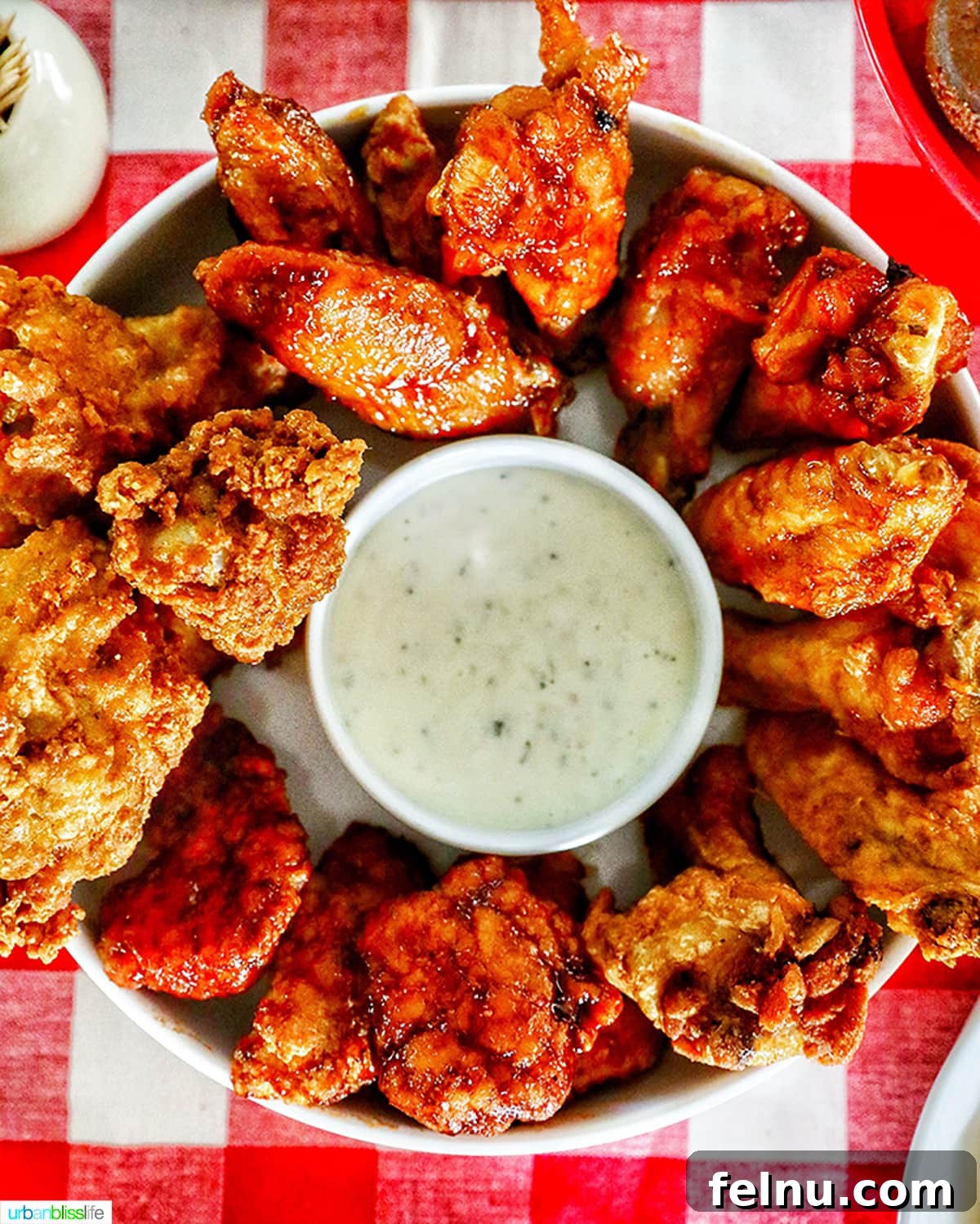 Ultimate Tailgate Grub Guide 4 A close-up shot of a plate of delicious chicken wings with various dipping sauces, set against a classic red and white checkered tablecloth.