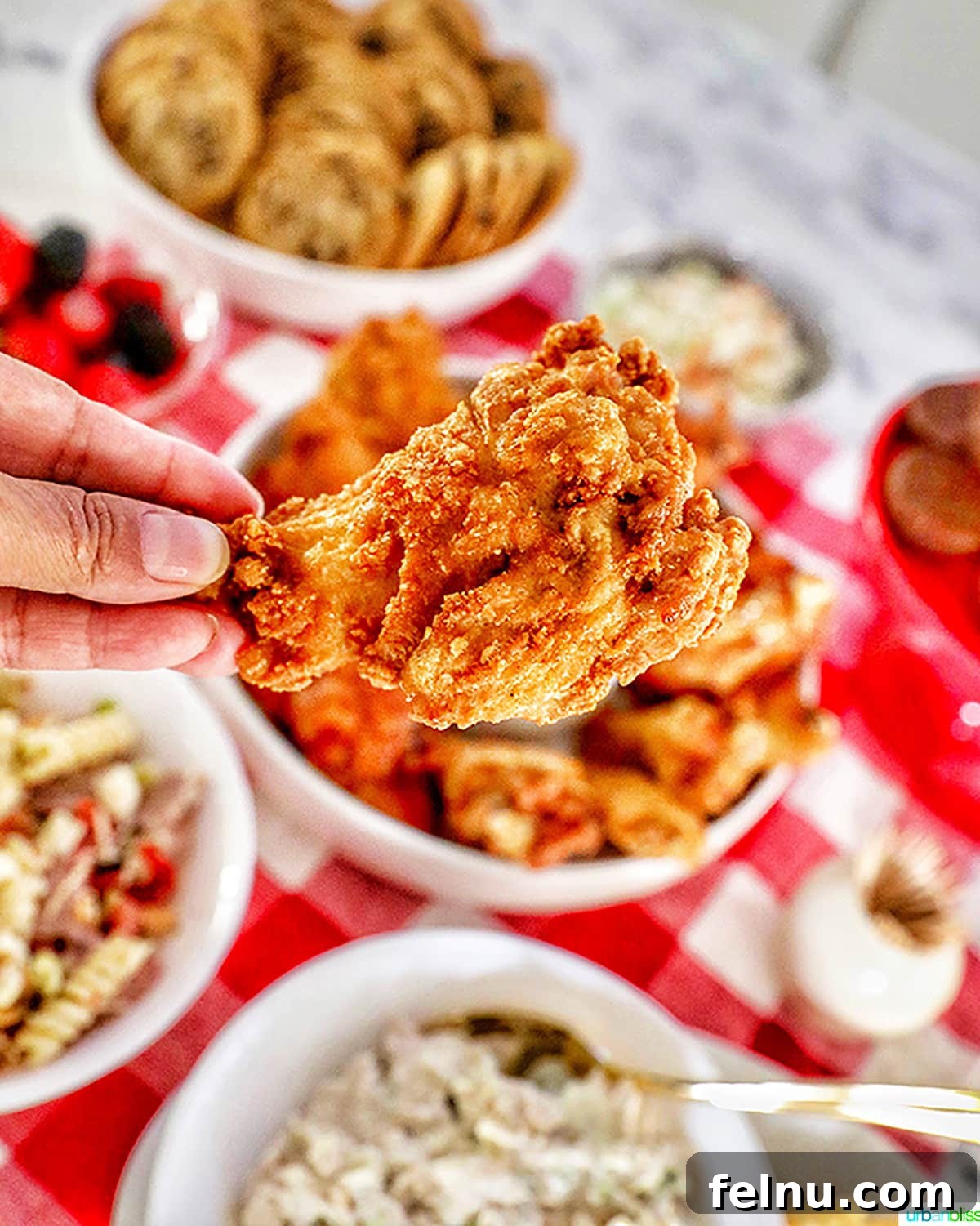 Ultimate Tailgate Grub Guide 9 A close-up shot of a person holding a crispy fried chicken wing, with a blurred background showcasing the rest of the tailgating food spread.