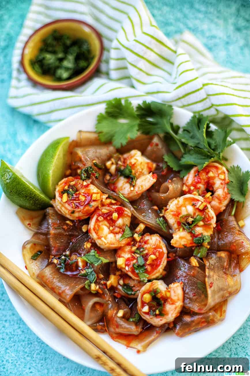 Spicy Lime Shrimp Glass Noodle Bowl 3 wide glass noodles with shrimp and chili lime oil sauce in a bowl with chopsticks, ready to eat