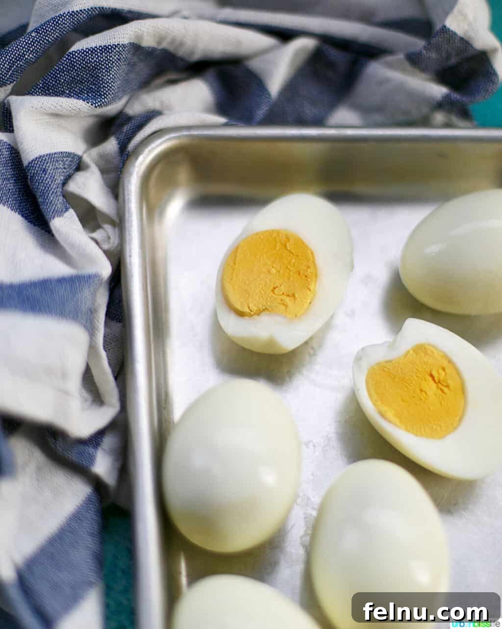 Perfect Hard Boiled Eggs with Ninja Foodi 9 Hard boiled egg cut open on a baking sheet, with several whole eggs around it