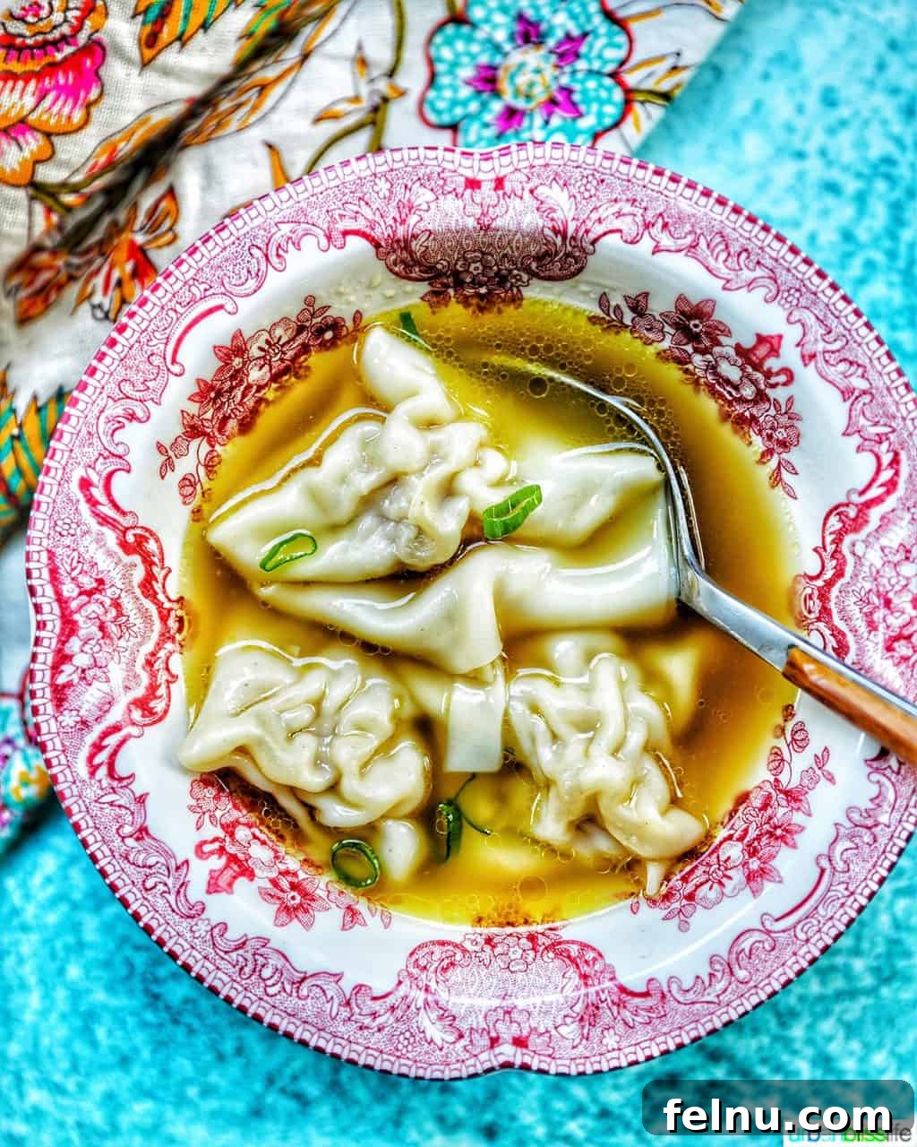 Mastering Ninja Foodi Pressure Cooker Meal Prep Cookbook 20 A single bowl of wonton soup with a spoon, on a colorful napkin with a blue background.