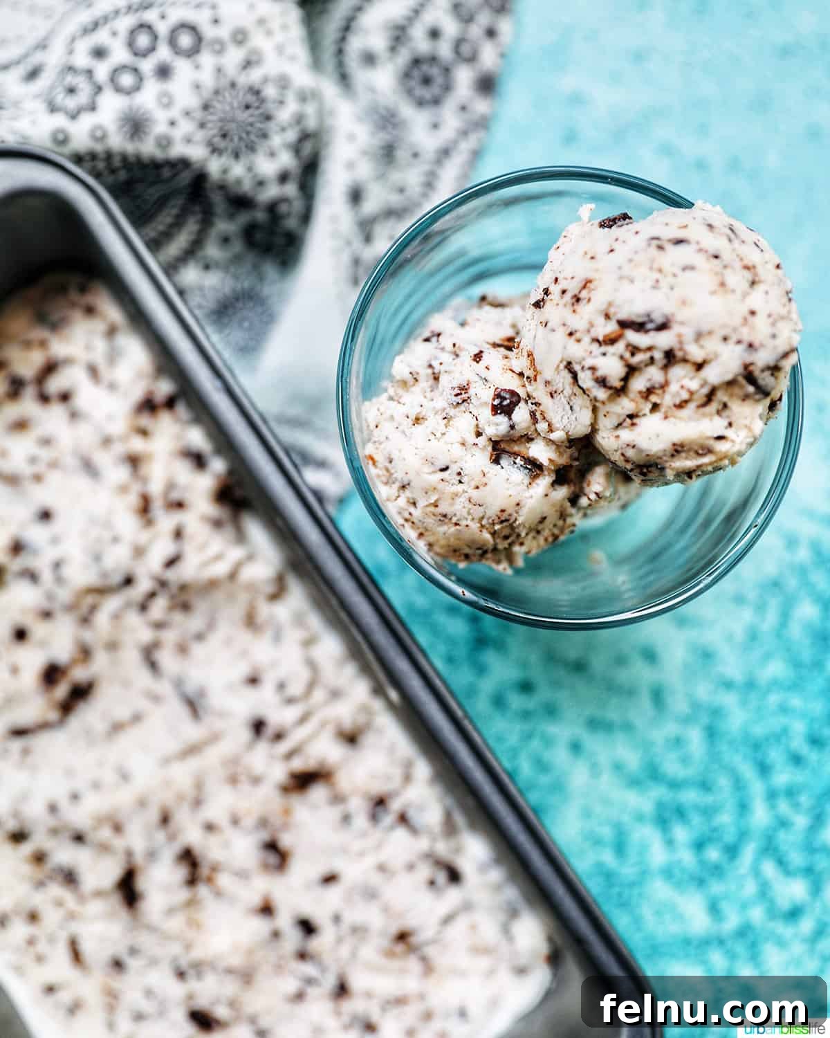 Decadent Dairy-Free Chocolate Chip Delight 2 Scoop of creamy dairy-free chocolate chip ice cream next to a pan of ice cream on a vibrant blue background, showcasing its rich texture.