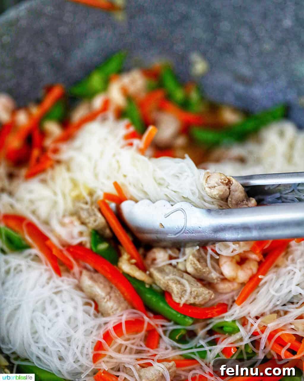 Filipino Pancit Bihon Delight 12 Mixing noodles into Filipino Pancit Bihon with tongs.