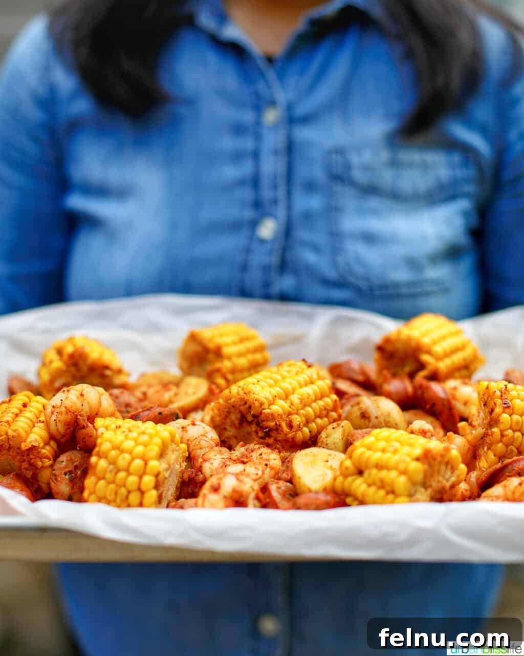 Folyoda Deniz Mahsulleri Şöleni 6 holding a tray of low country seafood boil foil packets against denim shirt