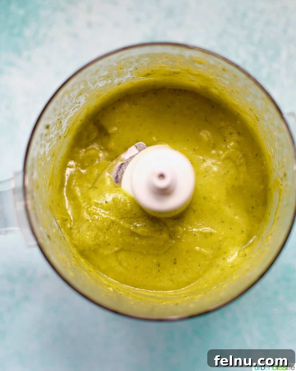 Creamy, vibrant green avocado sauce in a food processor after being blended.