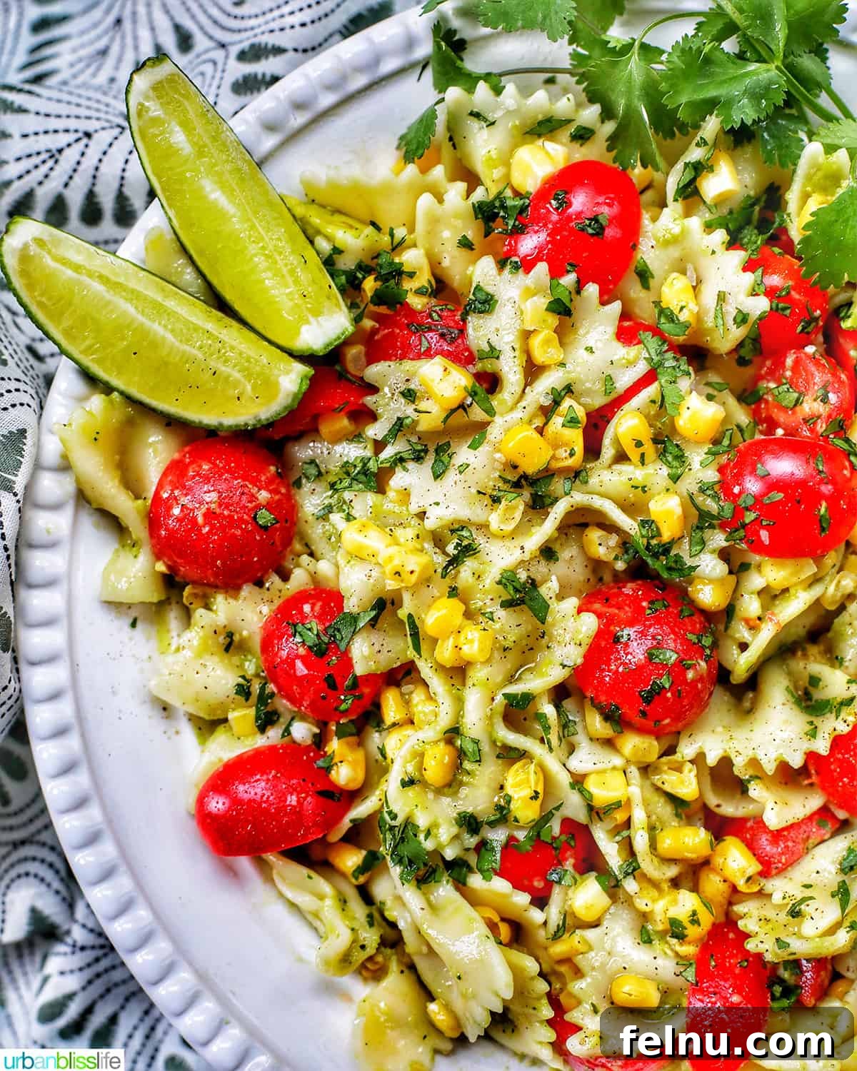 Close-up shot of the finished Avocado Pasta Salad with Tomatoes and Corn, garnished with lime wedges and fresh cilantro.