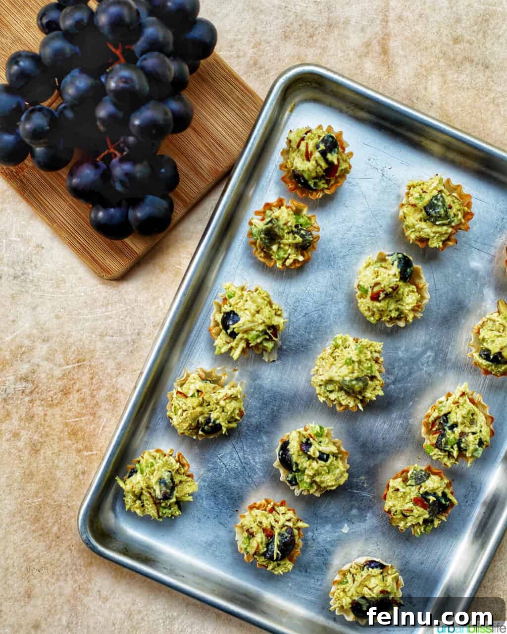 Golden Curry Chicken Salad with Grapes 9 A baking sheet filled with perfectly arranged curry chicken salad bites in phyllo shells, garnished with fresh grapes, showcasing their golden appearance before baking.