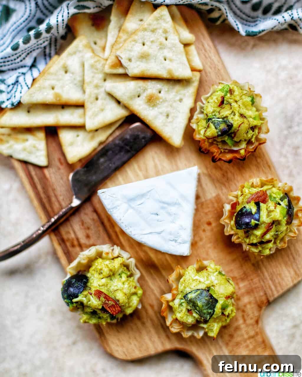 Golden Curry Chicken Salad with Grapes 10 A rustic cutting board laden with various snacks, including small plates of curry chicken salad with grapes, alongside cheeses, crackers, and other appetizers, creating a festive spread.